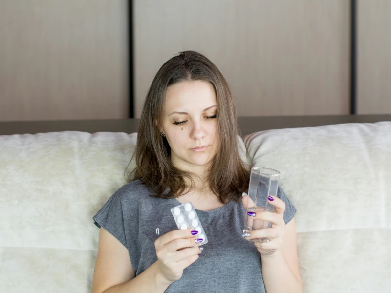 Frau im Bett mit Wasserglas und Tablettenblister